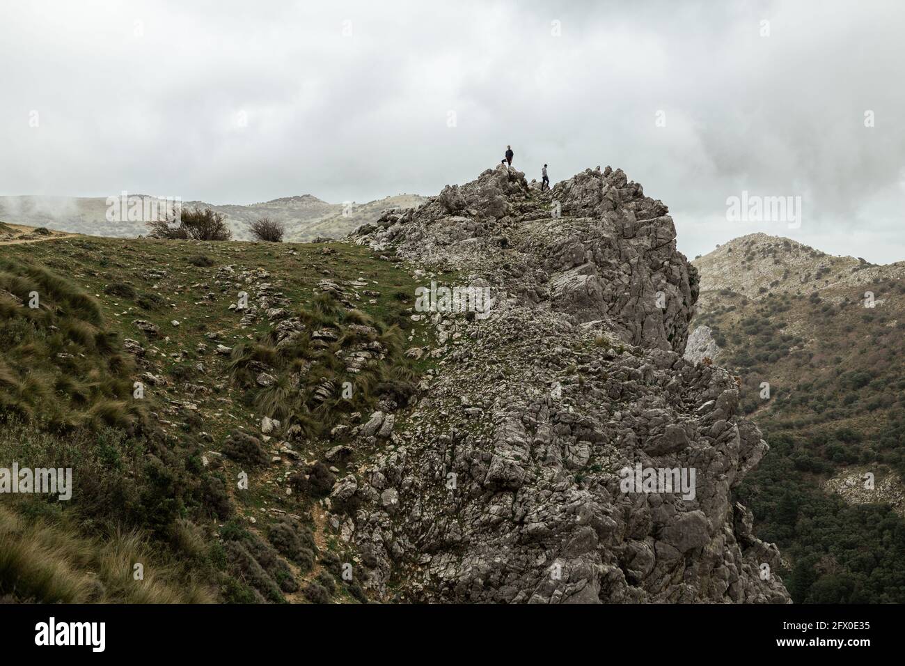 Weit entfernte Wanderer stehen auf rauem felsigen Berggipfel und bewundern highlands Landschaft unter bewölktem Himmel Stockfoto