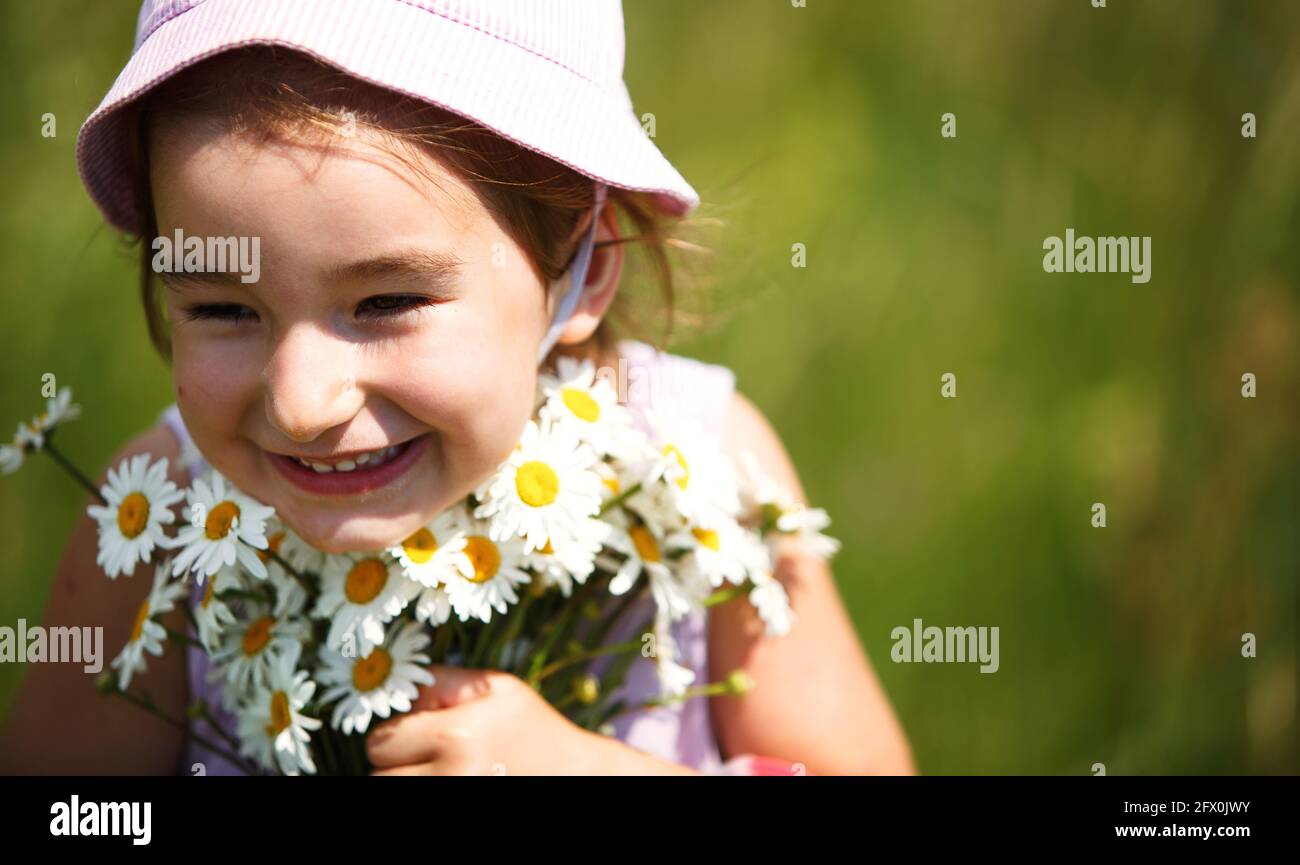 Kleines Mädchen mit einem Blumenstrauß von Gänseblümchen im Sommer auf einem natürlichen Hintergrund. Glückliches Kind, panamahut für Sonnenschutz. Internationaler Kindertag. Kopieren Stockfoto