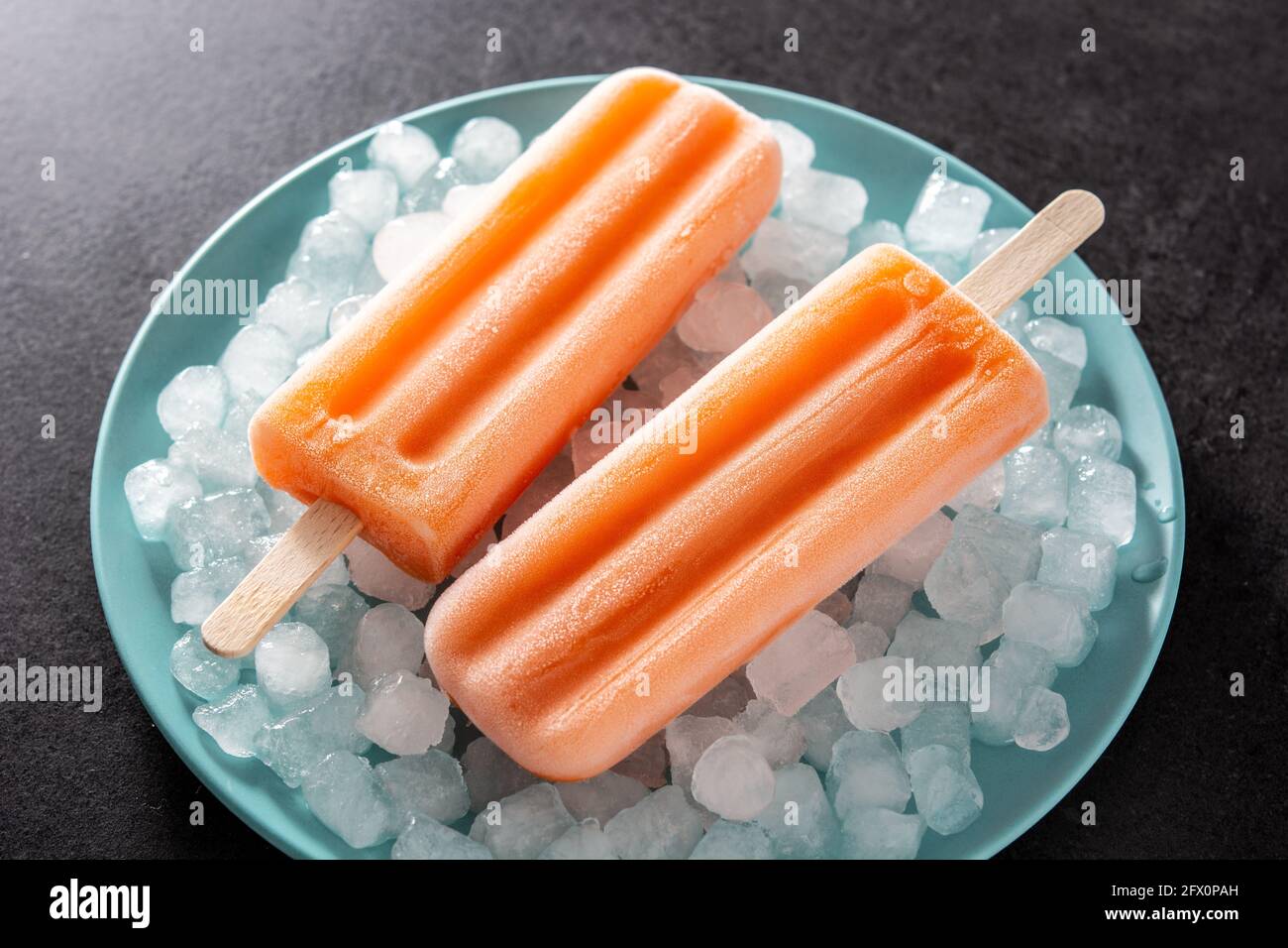Orangefarbene Eiszapfen auf blauer Platte auf schwarzem Hintergrund Stockfoto