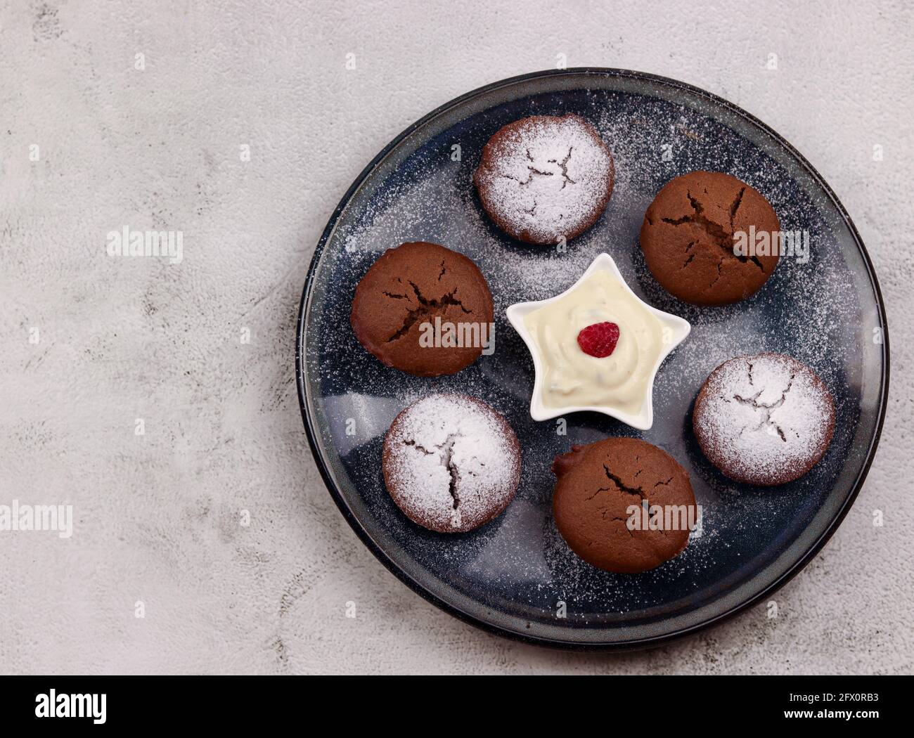 Kakao-Muffins mit Joghurt auf einem runden Teller auf hellgrauem Hintergrund. Draufsicht, flach liegend Stockfoto