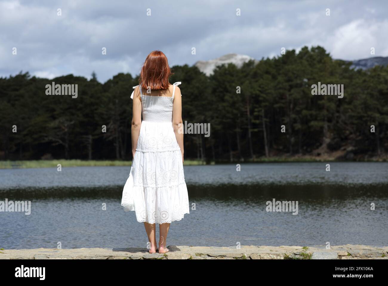 Rückansicht einer Frau in weißem Kleid, die Ansichten betrachtet In einem See stehen Stockfoto