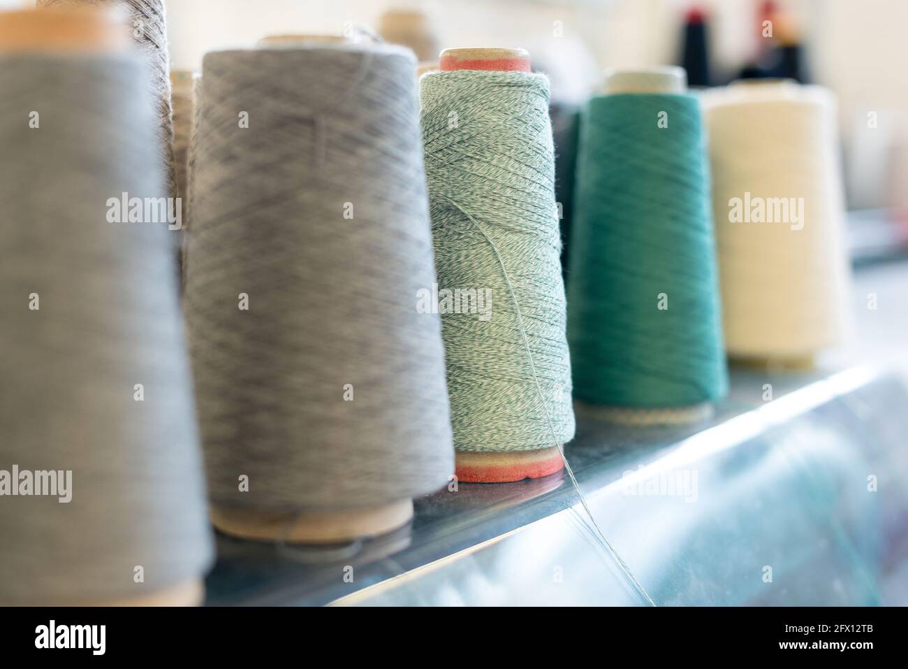 Zurückgehende Reihe von Kaschmirwolle auf konischen Spulen in Grün-, Grau- und Weißtönen in einer Strickfabrik mit Fokus auf eine Rolle grünen Garns im Cen Stockfoto