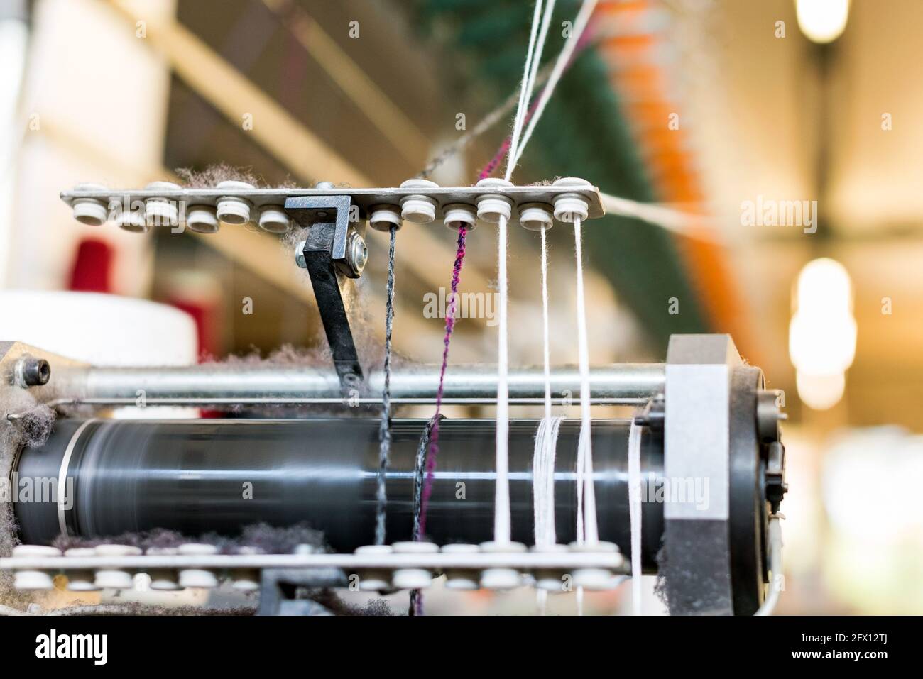 Nahaufnahme des farbigen Kaschmirwollgarns, das durch einen eingefädelt ist Zuführung auf einer handelsüblichen Strickmaschine in einem Strickwaren Fabrik Stockfoto