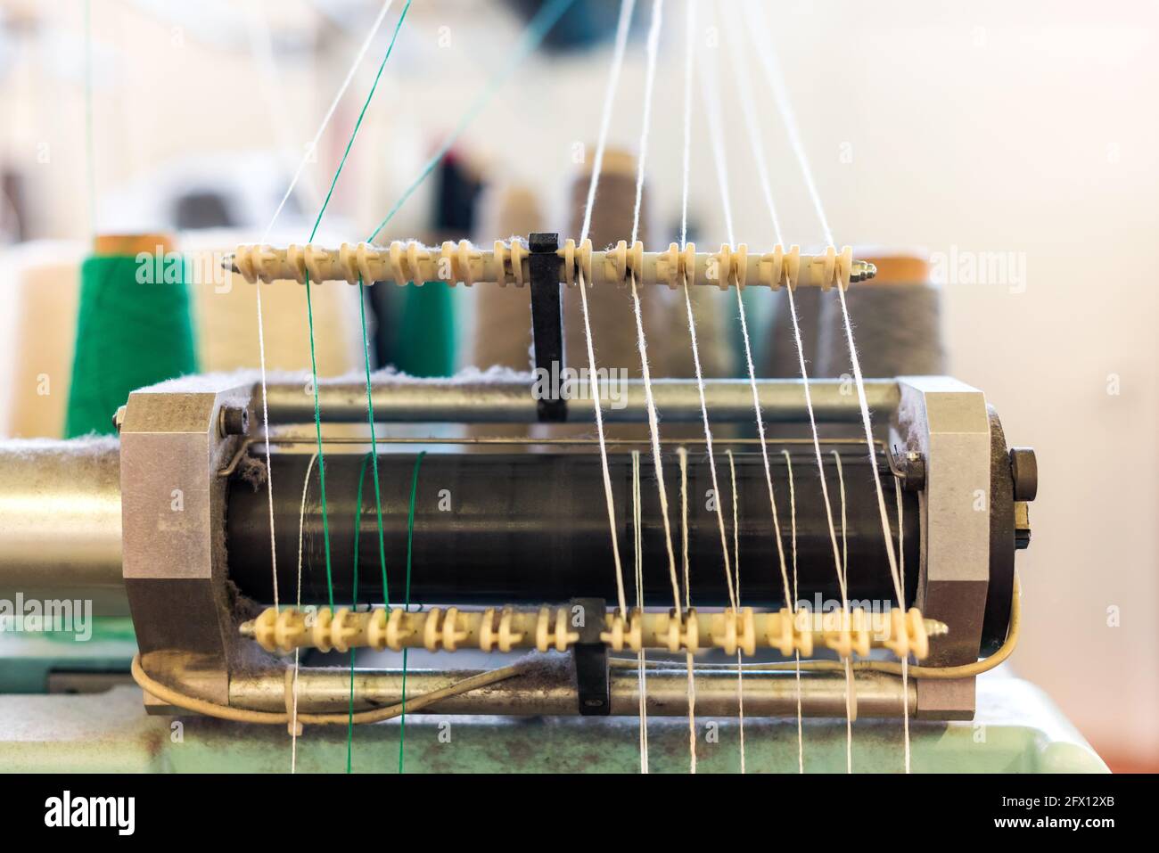 Nahaufnahme von grünen und weißen Kaschmirfäden im Zuführung an einer kommerziellen Strickmaschine in einer Strickfabrik In einem Produktionskonzept Stockfoto