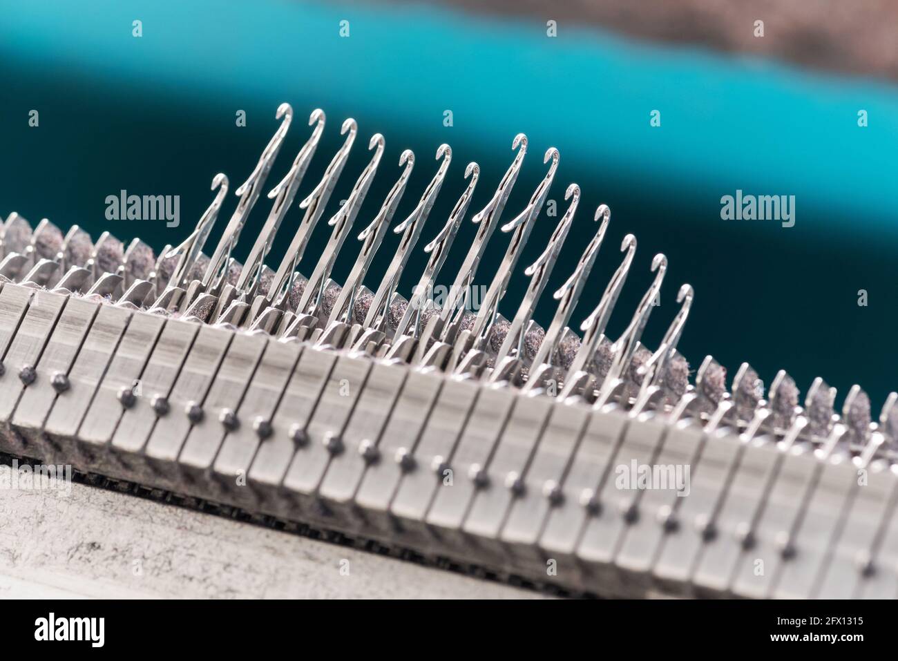 Nahaufnahme einer Reihe von hochgesteckten Stahlverriegelungen Nadeln auf einer handelsüblichen Strickmaschine in einer Strickfabrik Stockfoto