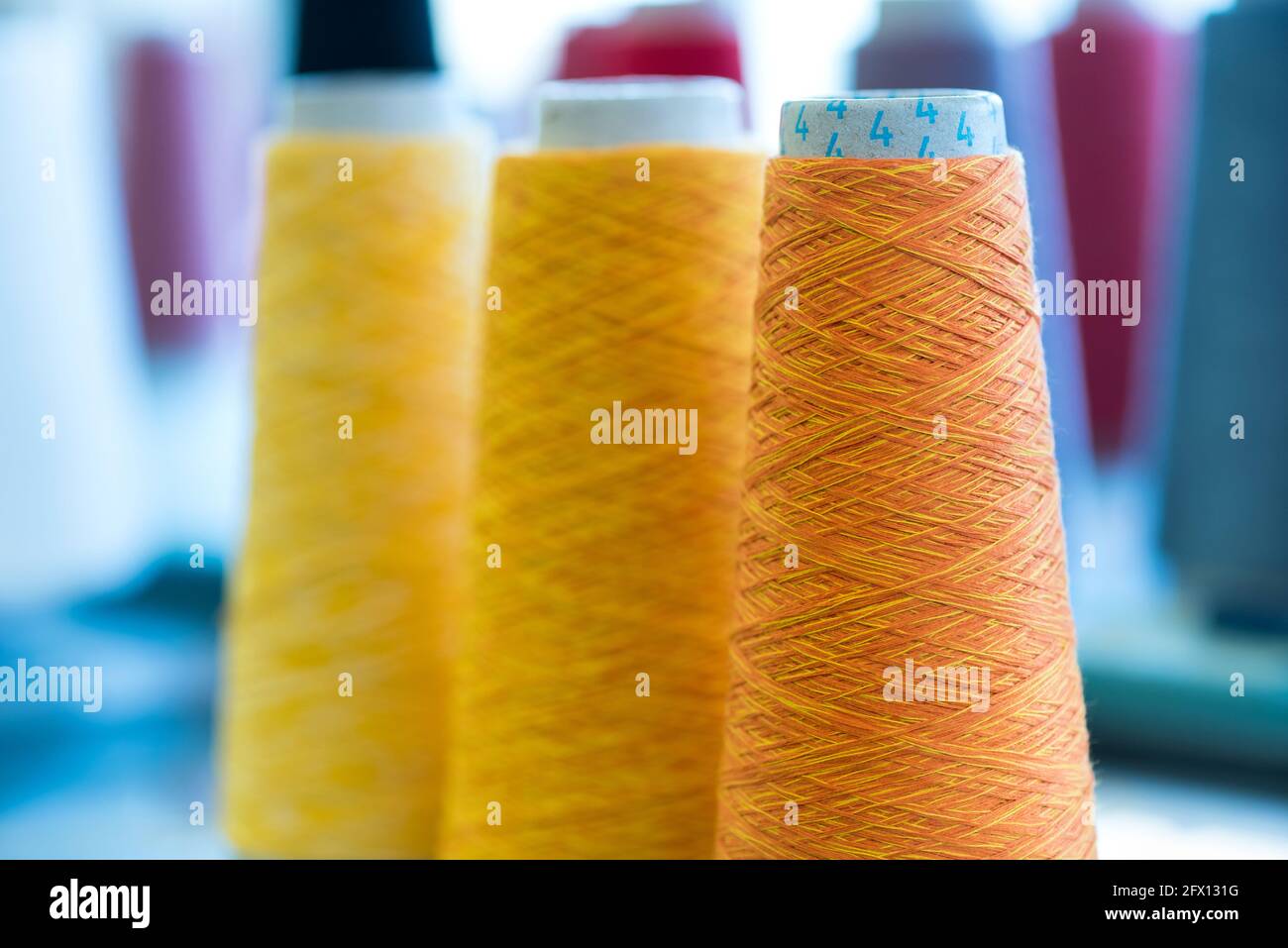 Drei konische Spulen aus buntem, gelbem und orangefarbenem Kaschmirgarn In einer Strickfabrik mit Fokus auf die orangene Rolle Im Vordergrund Stockfoto