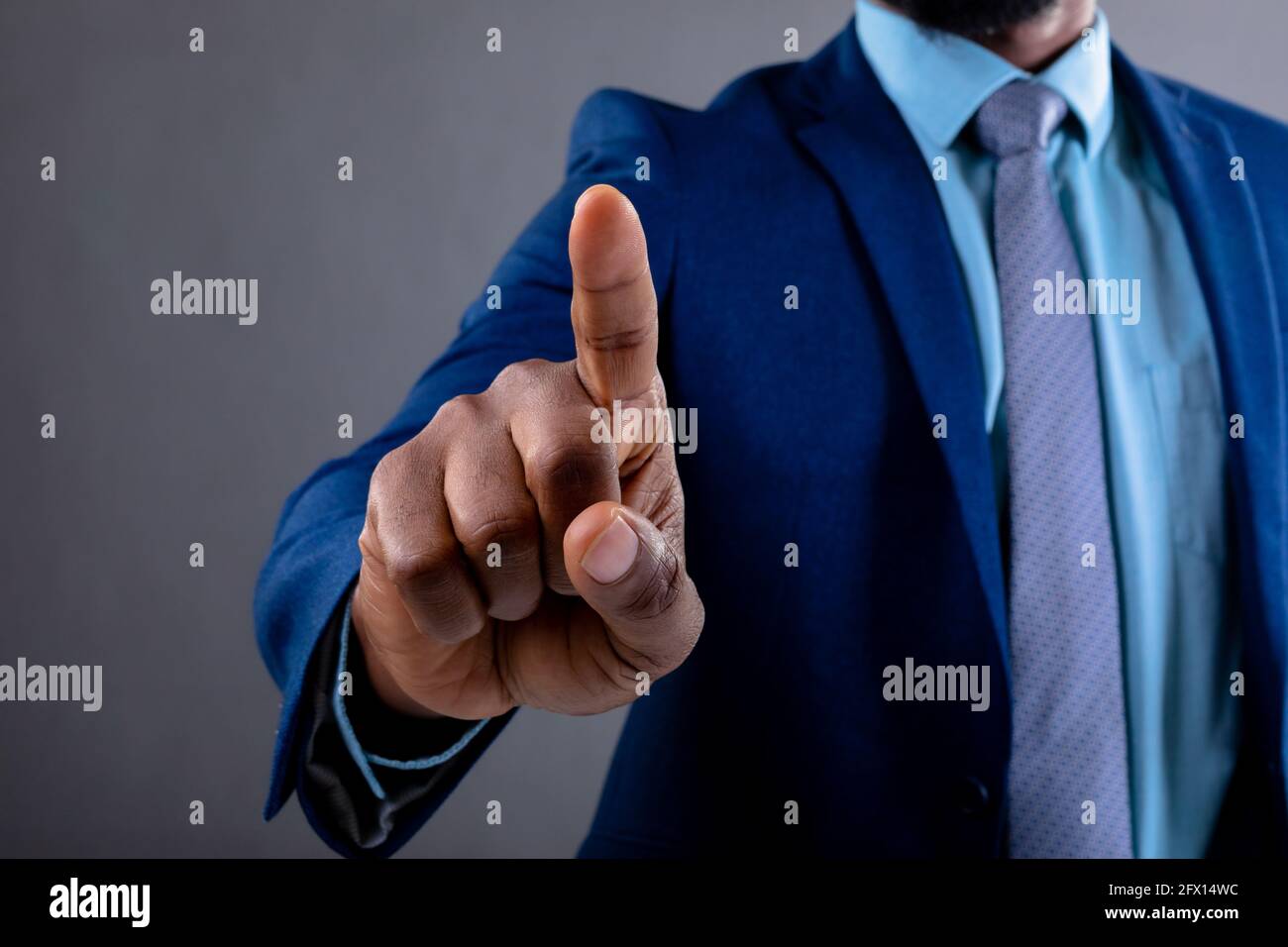 Mittelteil des afroamerikanischen Geschäftsmannes, der unsichtbaren Bildschirm berührt Grauer Hintergrund Stockfoto