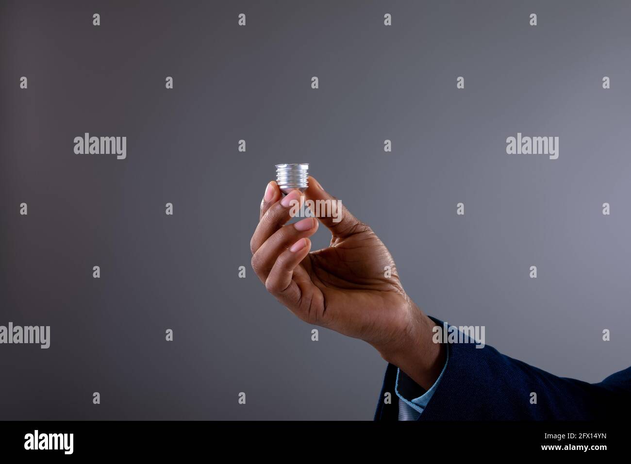 Nahaufnahme eines Geschäftsmannes, der den Sockel der Glühbirne gegen Grau hält Hintergrund Stockfoto