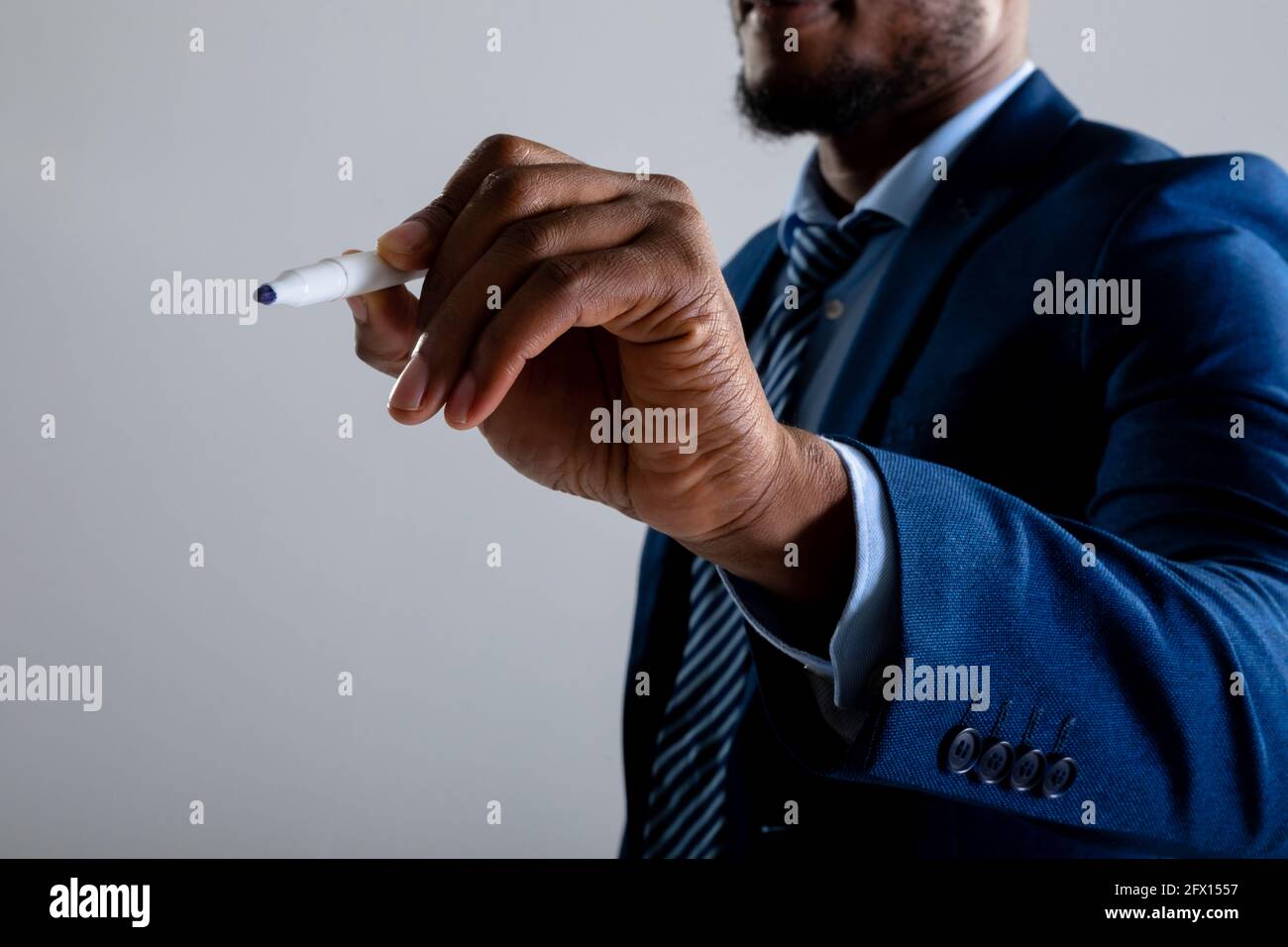 Mittelteil des Geschäftsmannes, der auf unsichtbarem Bildschirm gegen Grau schreibt Hintergrund Stockfoto