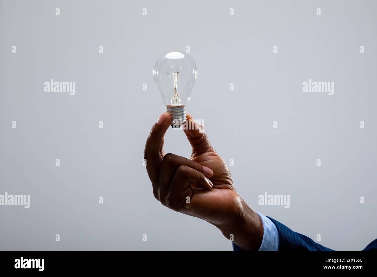 Nahaufnahme eines afroamerikanischen Geschäftsmannes, der eine Glühbirne gegen die Lampe hält Grauer Hintergrund Stockfoto