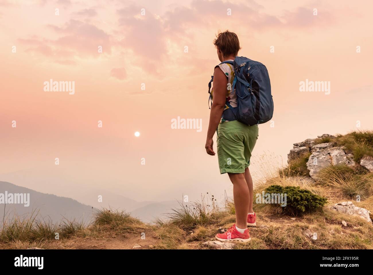 Ein Tourist mit Rucksäcken, der den Sonnenuntergang auf einem genießt Berg Stockfoto