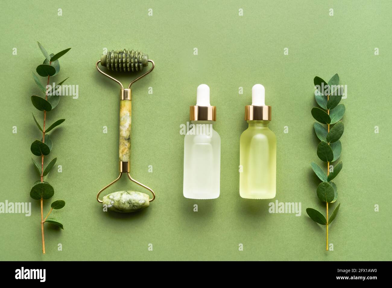 Grüne Massage-Walze mit Jade, Tropfflaschen aus Glas für medizinische und kosmetische Zwecke und Eukalyptus auf grünem Hintergrund. SPA-Konzept. Stockfoto
