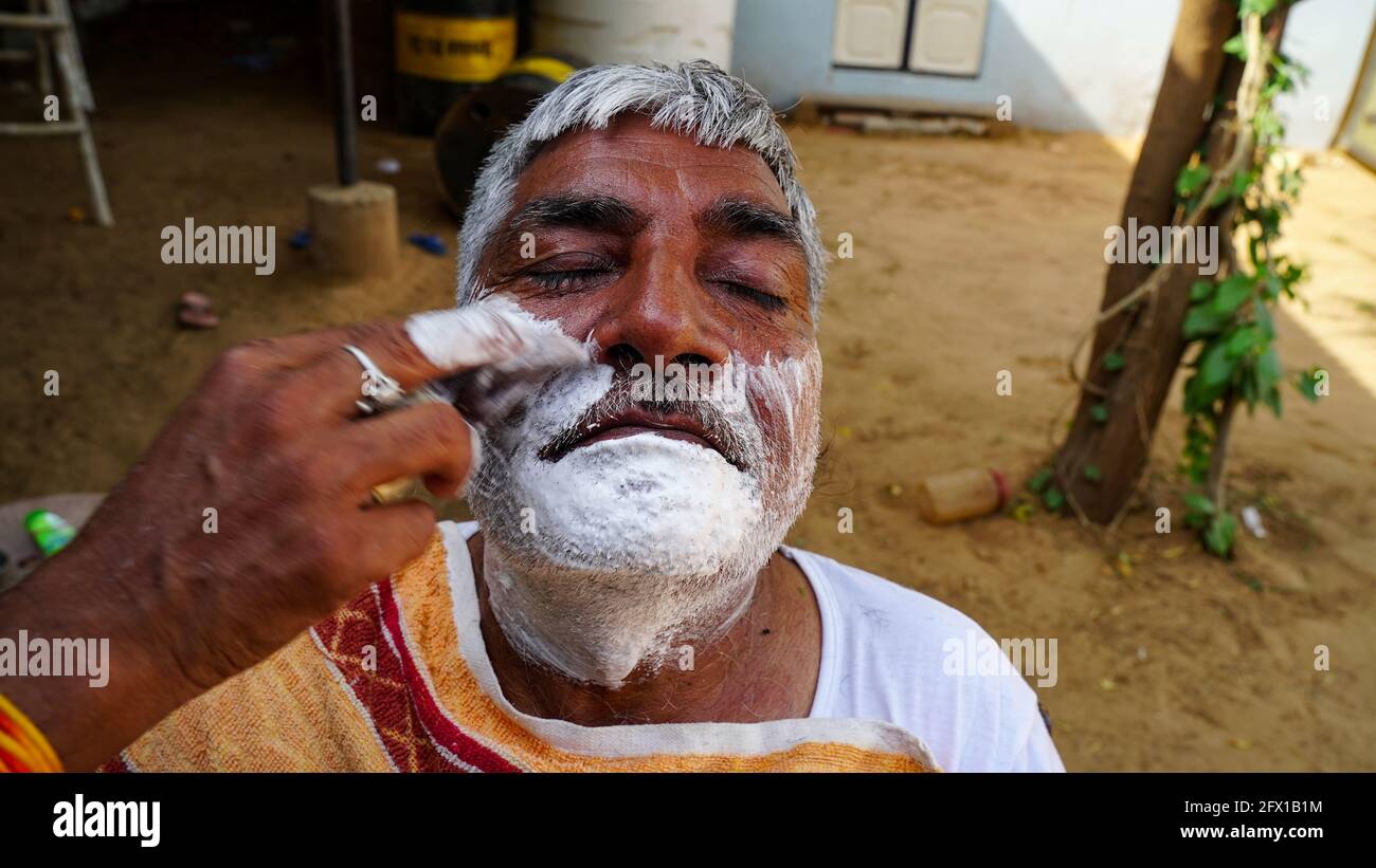 01. Januar 2021- Reengus, Sikar, Indien. Straßenbarbier, der einen Mann mit einer offenen Rasierklinge auf einer Straße in Sikar rasiert. Stockfoto