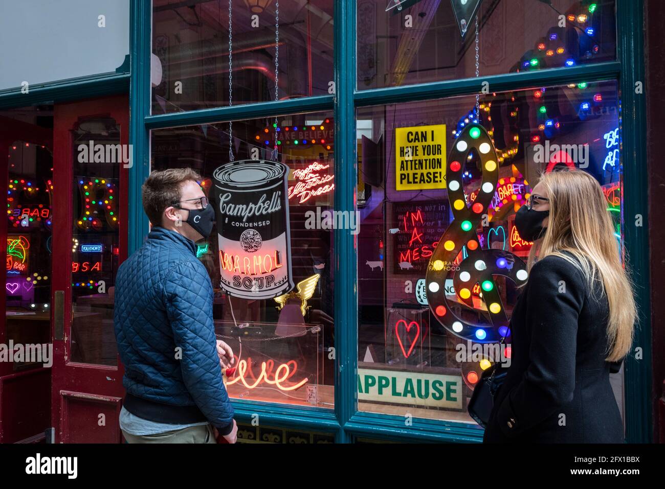 London, Großbritannien. 25 Mai 2021. Passanten sehen „Electric City“, eine Ausstellung im Leadenhall Market mit Neon- und Bühnenstücken, die von Gods own Junkyard, der seit über 40 Jahren an Filmsets arbeitet, für den Film gemacht wurden. Der Gründer Chris Bracey verstarb 2014 und das Unternehmen wird seitdem von seiner Frau Linda und den Söhnen Matthew und Marcus, allesamt Neon-Hersteller und -Designer, geführt. Vom 26. Mai bis zum 31. Juli werden Neon-Schilder von Stanley Kubricks Augen weit geschlossen, Richter Dredd, Batman, Tomb Raider, Charlie und der Schokoladenfabrik und dem Dunklen Ritter gezeigt. Kredit: Stephen Chung / Alamy Live Nachrichten Stockfoto