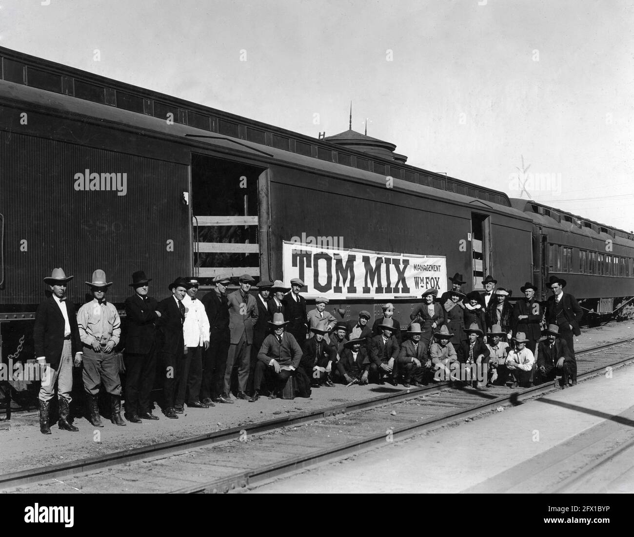 TOM MIX (links vom Banner in weißer Mütze) Und seine Filmgesellschaft posiert vor den Santa Fe Train-Waggons Circa 1925 Fox Film Corporation Stockfoto