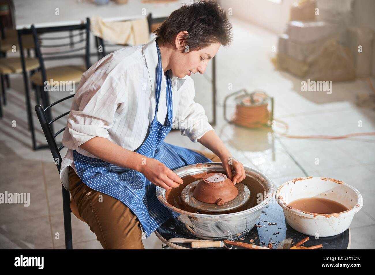 Fokussierte Frau, die eine Tonkugel an der Schalenseite am Rad befestigt Stockfoto