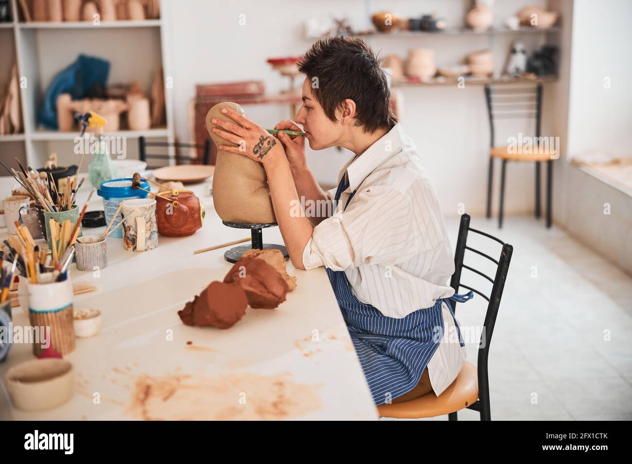 Töpferfachfrau, die mit ihrem Modellierwerkzeug präzise Schnitte macht Stockfoto