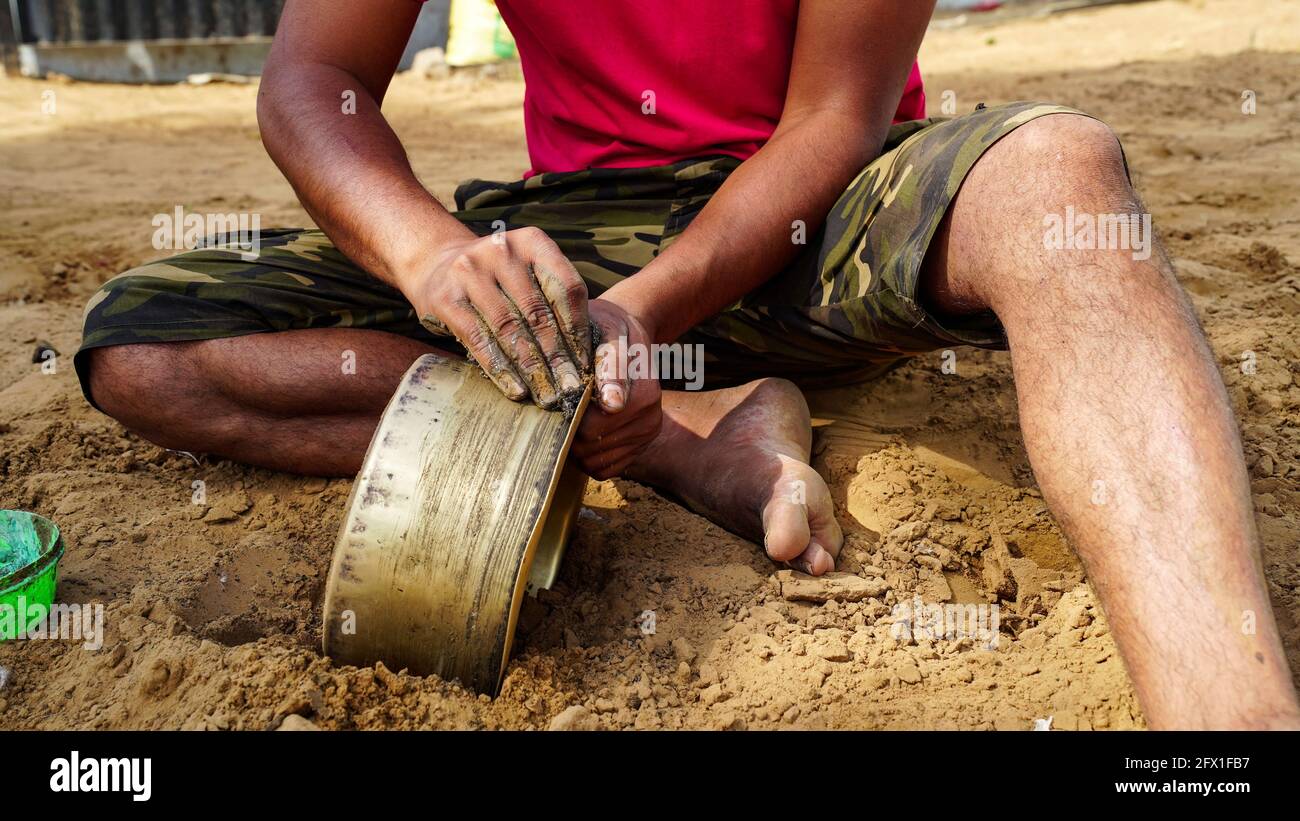 Nicht identifizierter indischer Mann, der Messingtopf mit reinem Boden reinigt. Indische ländliche Landschaft. Stockfoto