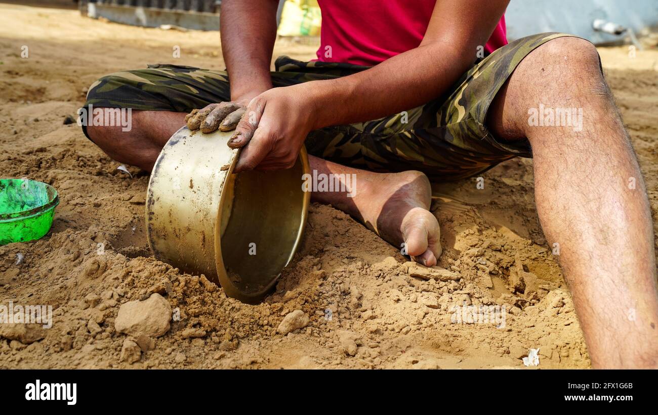 Nicht identifizierter indischer Mann, der Messingtopf mit reinem Boden reinigt. Indische ländliche Landschaft. Stockfoto