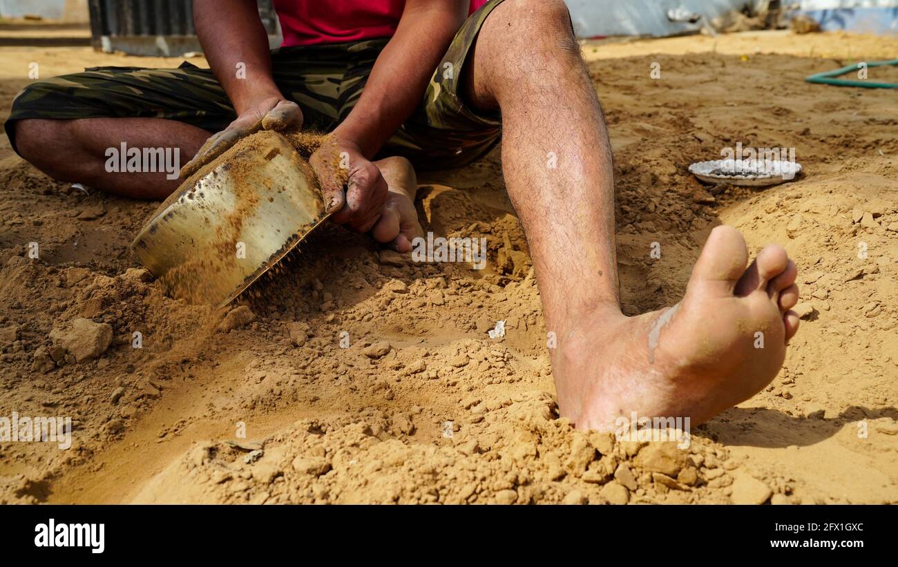 Junger Mann mit rotem Hemd versucht, einen Messingtopf mit Erde und Wasser zu reinigen. Reiner Boden ist am besten antibakteriell für die Reinigung Töpfe. Stockfoto