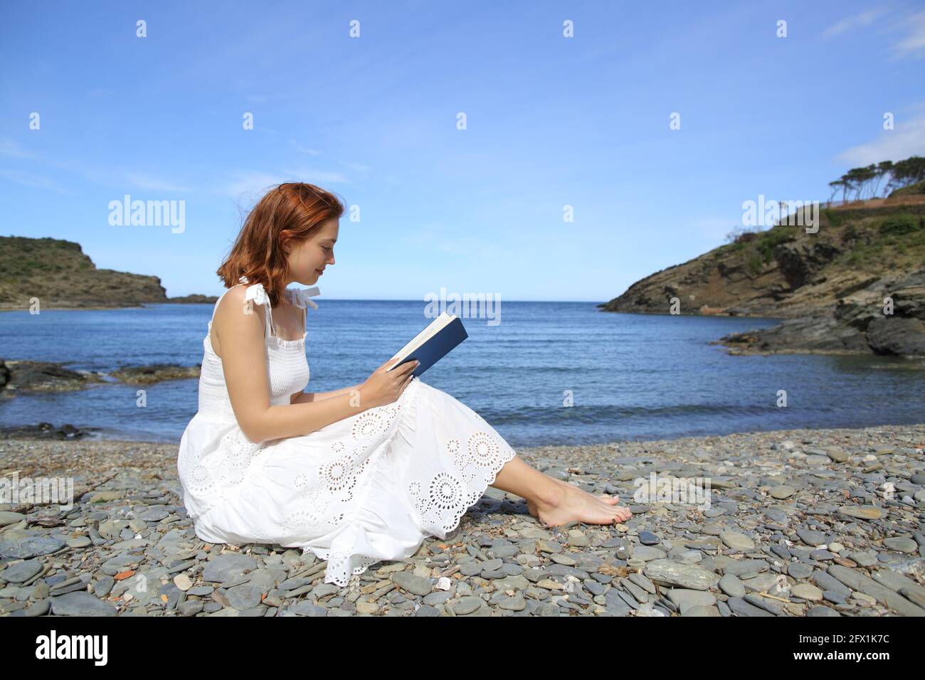 Seitenansicht Porträt einer Frau in weißem Kleid Lesung Ein Buch am Strand Stockfoto