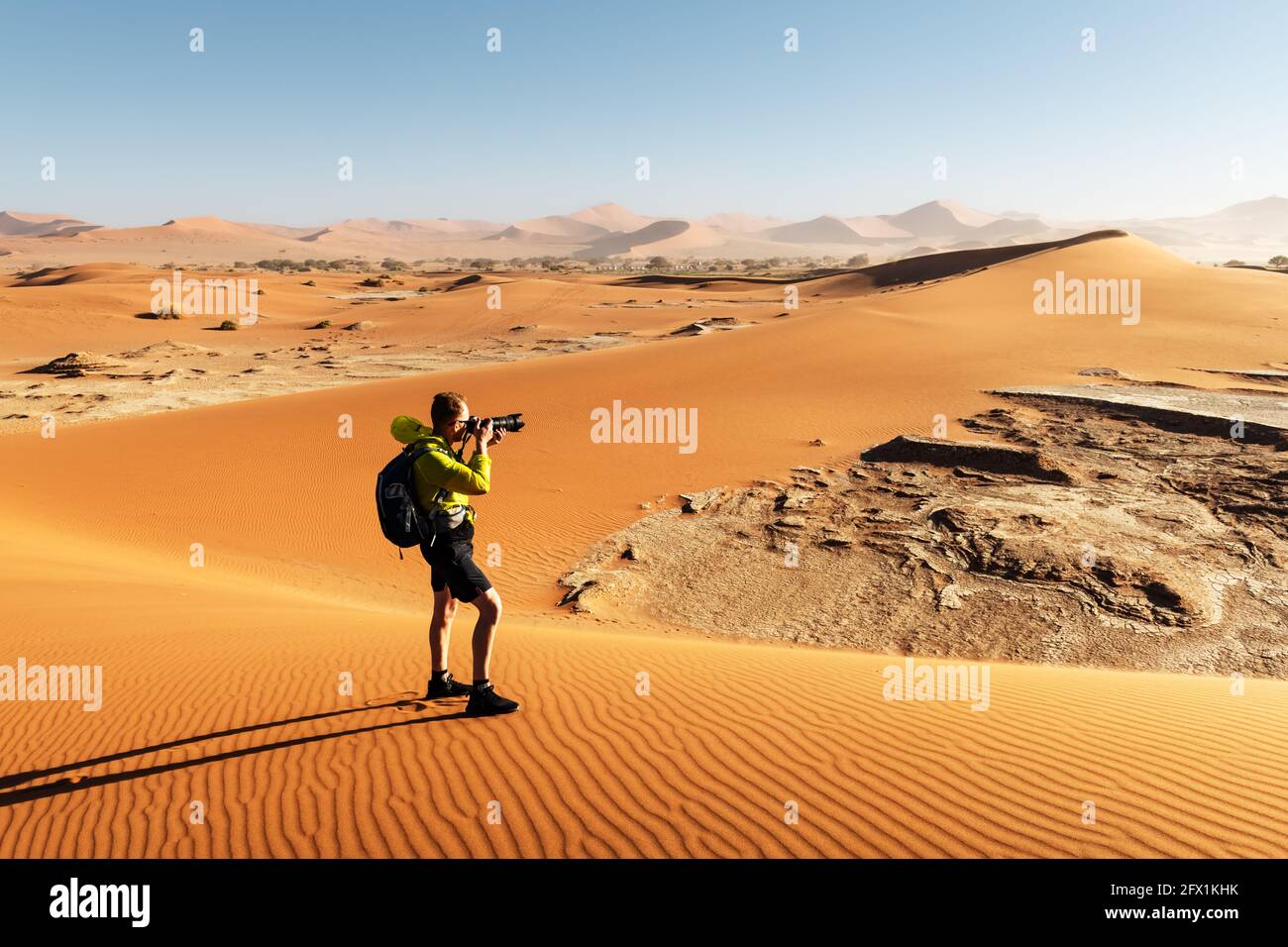Fotograf, der in Deadvlei, Namib-Naukluft Nationalpark, Namibia, Afrika fotografiert. Getrockneter Boden mit Sand in der Namib Wüste bei Sonnenuntergang. Landschaftsfotografie Stockfoto