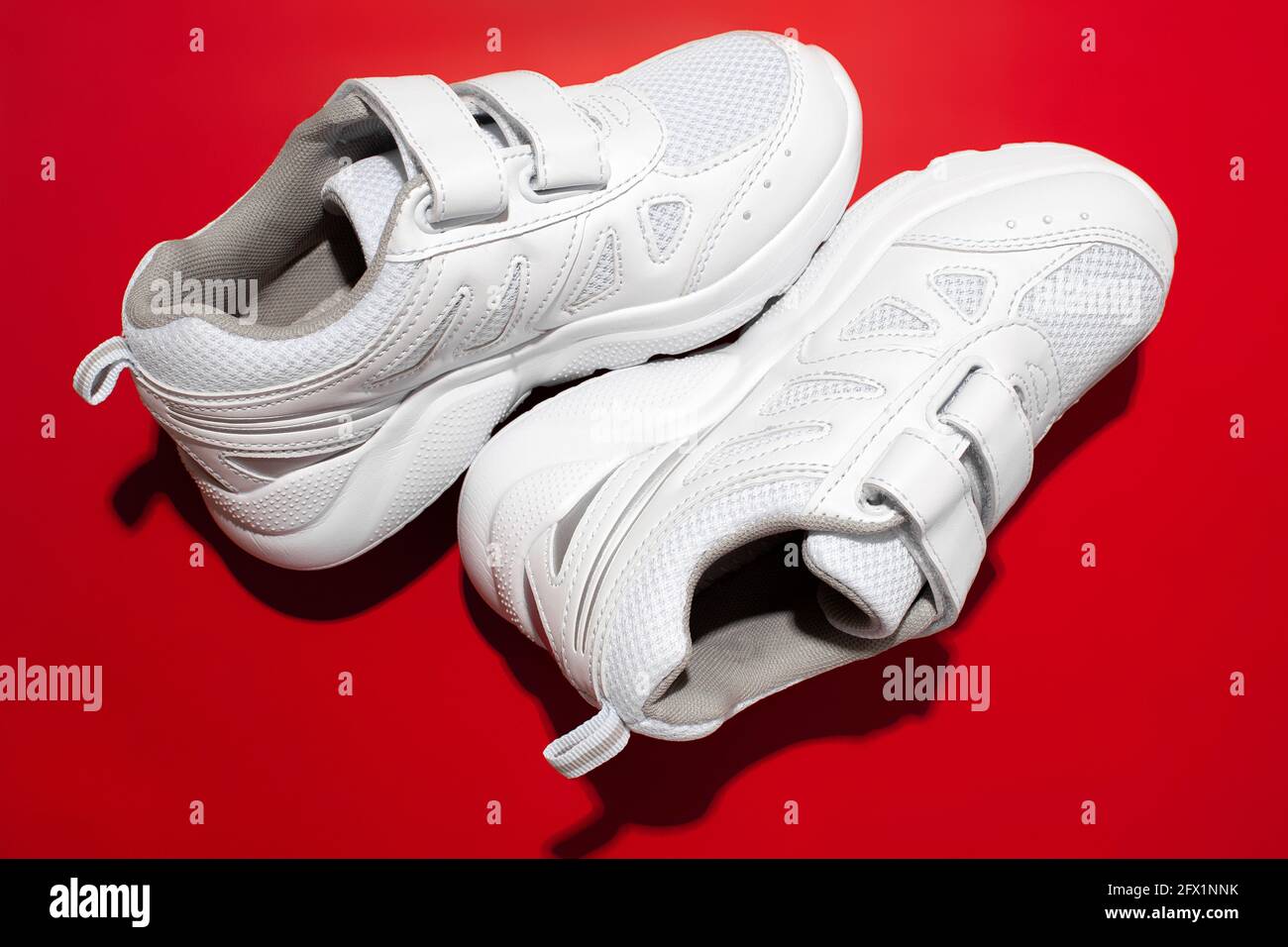Draufsicht Makro-Set Pyramide von zwei weißen Kinder Sneakers Mit Klettverschlüssen für bequemes Schuhwerk isoliert auf einem roten Hintergrund mit einem harten Stockfoto