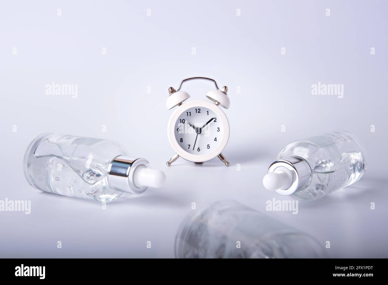 Rund um die Uhr liegen Flaschen mit Gesichtsserum auf einem weißen Tisch. Das Konzept des Ausscheides der Jugend. Erhalten Sie die Hautfestigkeit. Stockfoto