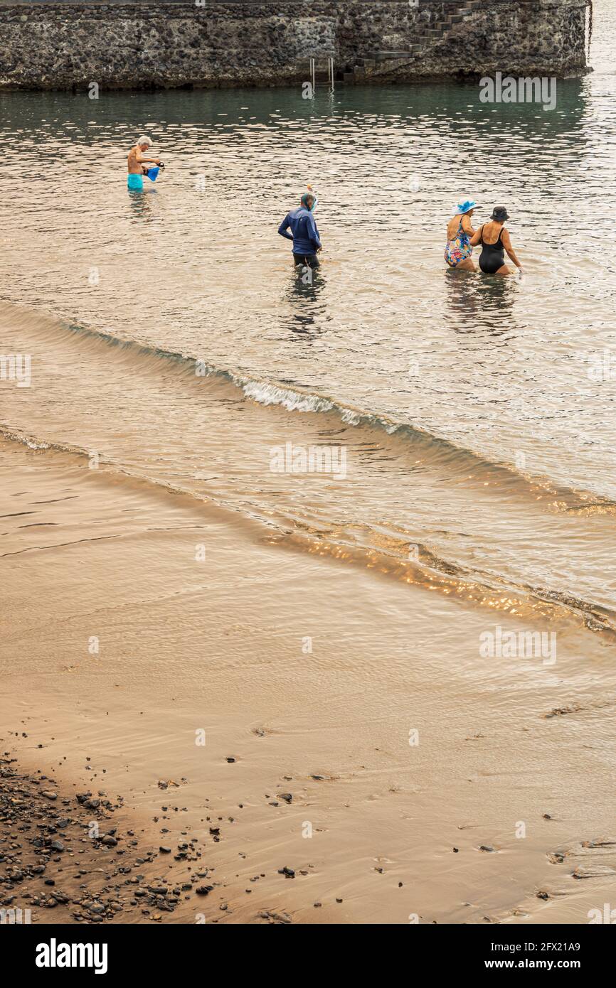 Menschen betreten das Wasser unter einem seltsamen Licht, das durch den Rauch eines Waldbrands verursacht wird, der die Sonne blockiert, Playa San Juan, Teneriffa, Kanarische Inseln, Spanien Stockfoto