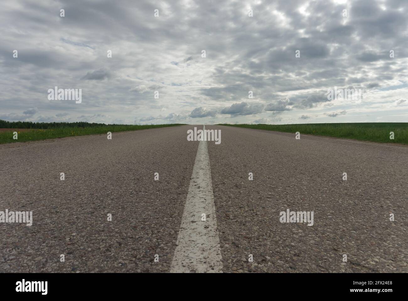 Low-Angle-Ansicht der Mittellinie auf einem leeren Ländliche Asphalt oder geteerte Straße in einem abnehmenden oder zurückgehenden Perspektive zwischen grünen Feldern unter einer Wolke Stockfoto