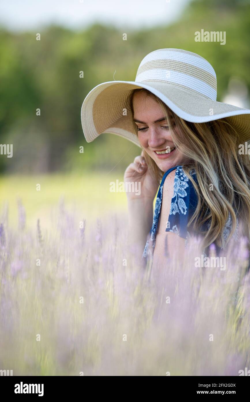 Schöne junge Frau mit einem Floppy-Sonnenhut sitzt in einem frischen Lavendelfeld. Blühende Wiese, Landschaft Landschaft Bokeh Hintergrund Stockfoto