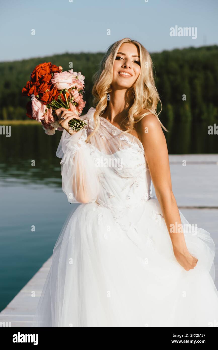 Elegante blonde Braut in Weiß mit einem Hochzeitsstrauß gekleidet. Hochzeitskonzept Stockfoto