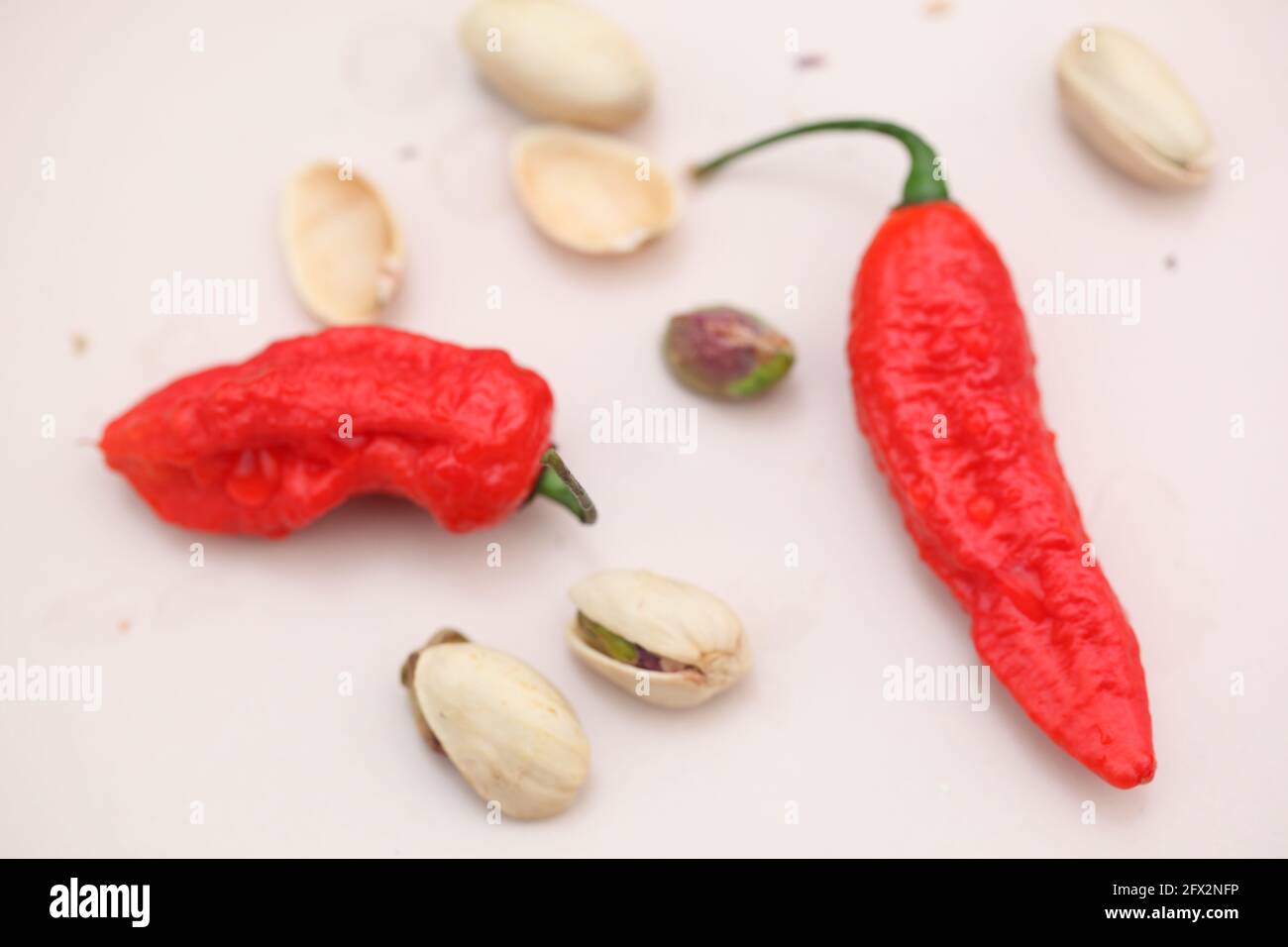 Blick auf Red Hot Chilis und Pistazien auf cremig Hellrosa Keramik Stockfoto