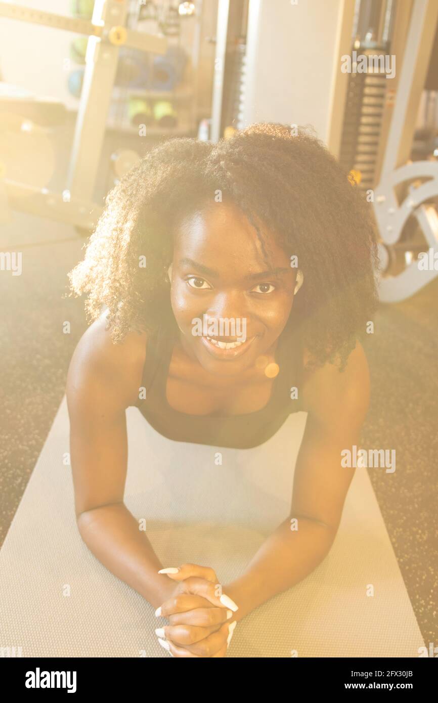 Leuchtende junge Frau auf einer Yogamatte beim Training. Nahaufnahme, Blick auf Kamera, Fitness, Arme Kreuz, Afroamerikaner, Schwarze Frau, Portrait, Yogamatte Stockfoto