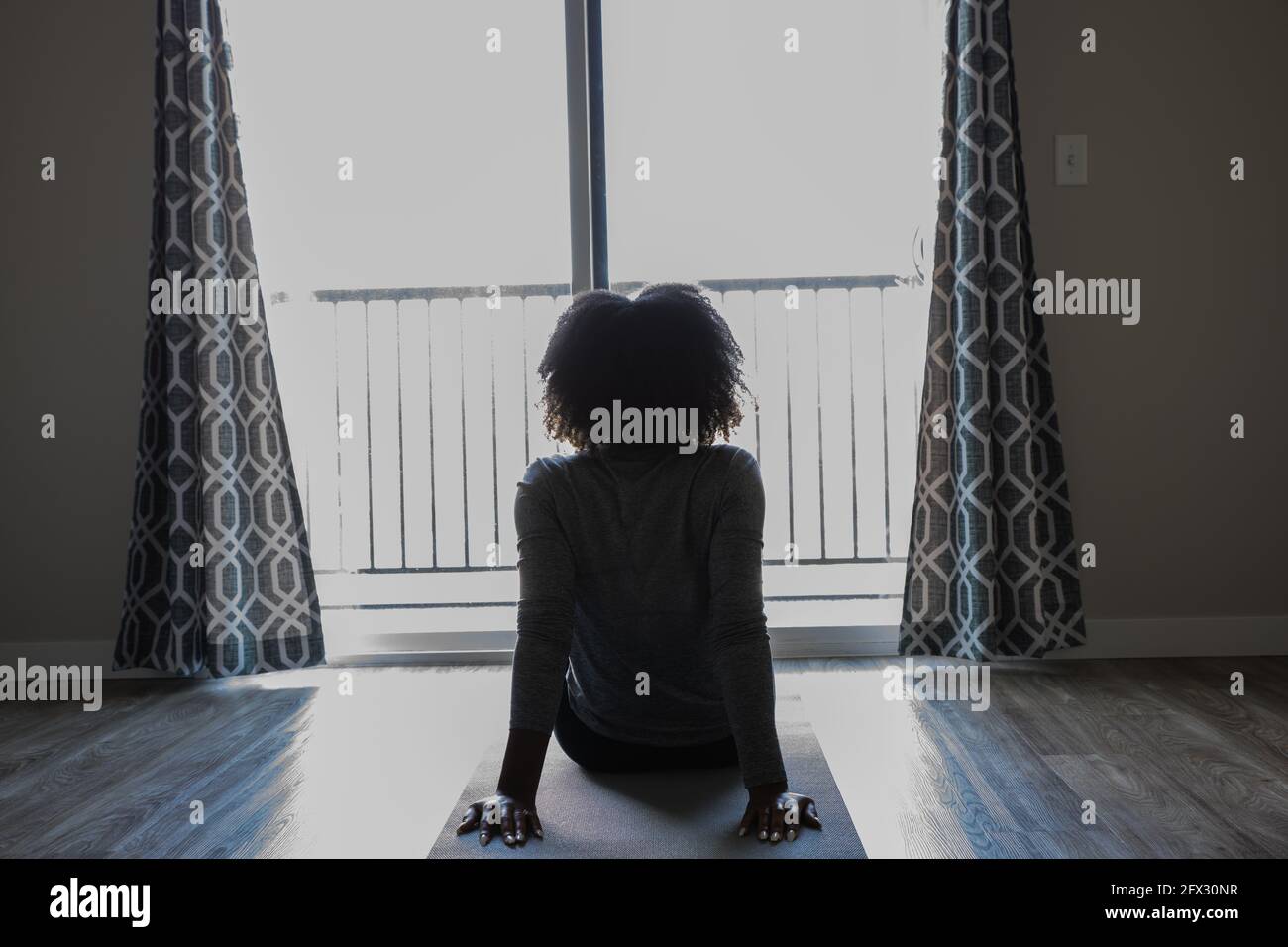 Eine Frau, die auf einer Yogamatte sitzt und aus dem Fenster schaut, eine Person, aus der Nähe, afroamerikanerin, schwarze Frau, Fitness, meditieren, isolieren, gesund li Stockfoto