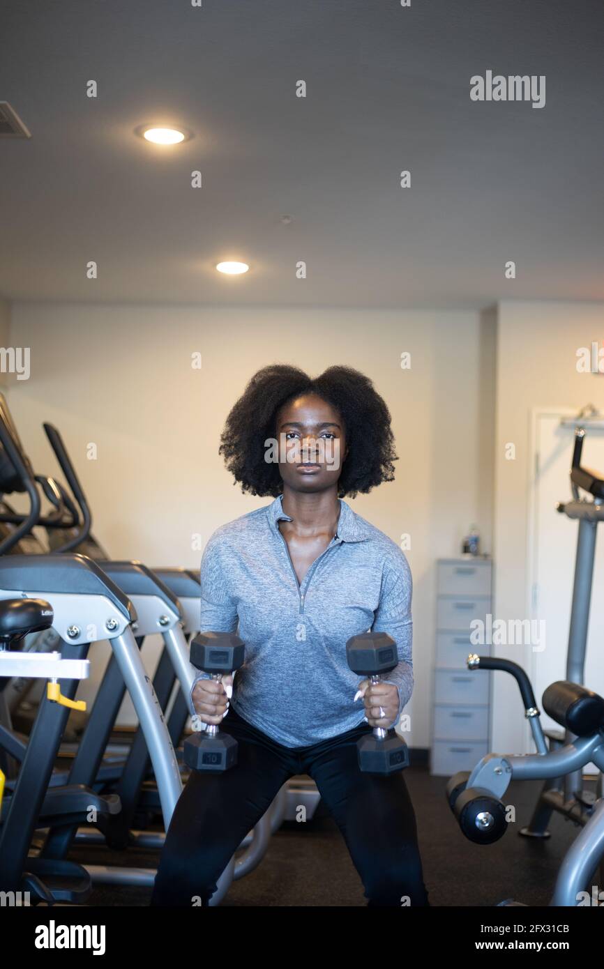 Junge Frau tut Ausfallschritte und hocken Übung im Fitnessstudio. Nahaufnahme, eine Person, afroamerikanisch, schwarze Frau, Fitness, Hintergrund, Kurzhanteln, natürliche Haare, Stockfoto