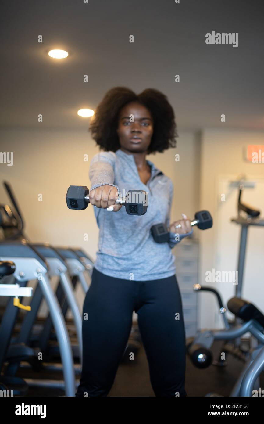 Frau beim Training mit Hanteln im Fitnessstudio zu Hause. Nahaufnahme, eine Person, Fitnessmodell, afroamerikanisch, afrikanisches Modell, Sportbekleidung, Naturhaar-Modell Stockfoto
