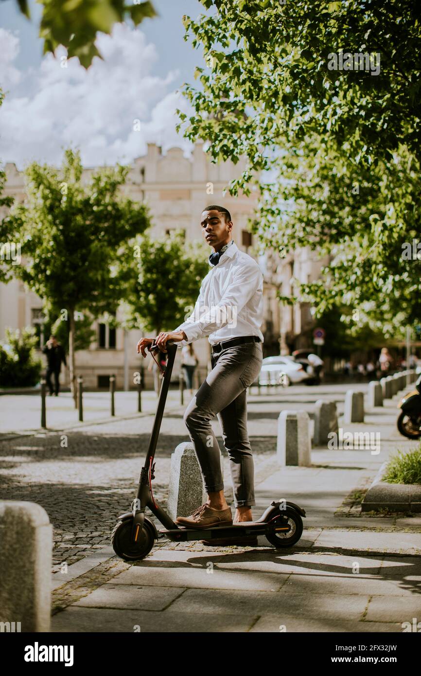 Hübscher junger afroamerikanischer mit Elektroroller auf einer Straße Stockfoto