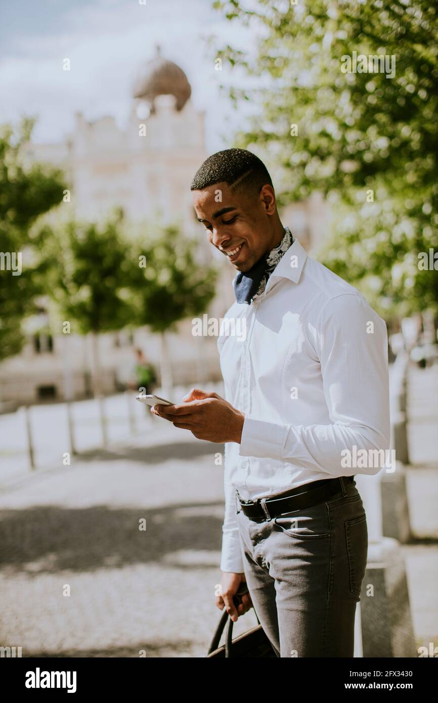 Hübscher junger afroamerikanischer Geschäftsmann, der ein Mobiltelefon benutzt Warten Sie auf ein Taxi auf einer Straße Stockfoto