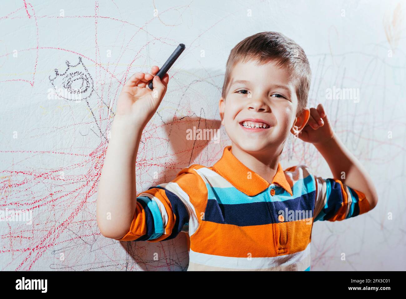 Lachendes Kind zeichnet mit Buntstiften an die Wand Stockfoto