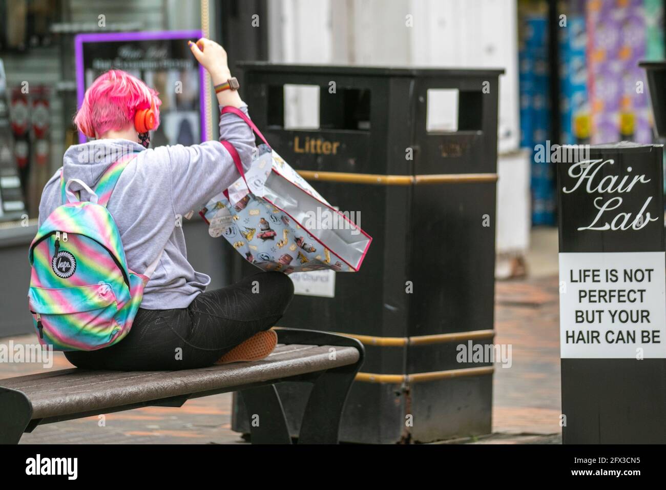 „Frau, mit rosa gefärbten Haaren, die außerhalb des Haarlabors sitzen, weibliche Friseurladen im Stadtzentrum von Preston, Großbritannien das Leben ist nicht perfekt, aber dein Haar kann es sein“ Stockfoto