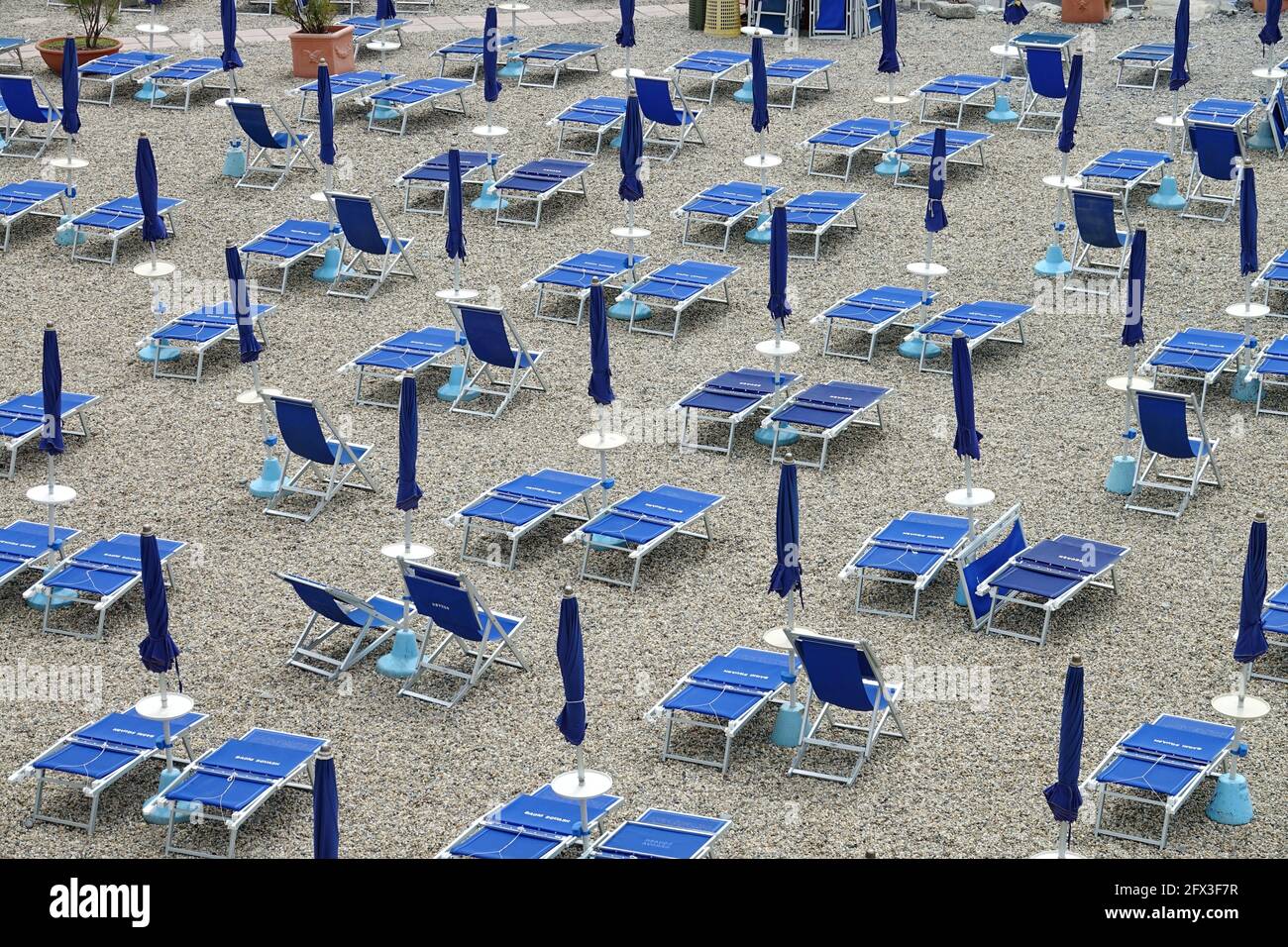 Leere Strandliegen mit eingeklappten Sonnenschirmen in Italien Stockfoto