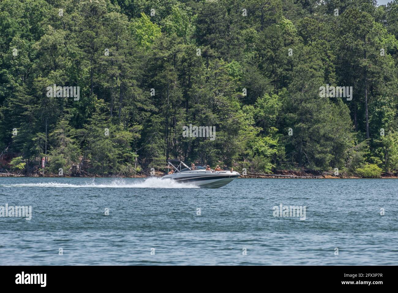 Eine Gruppe junger Menschen genießt eine Fahrt mit dem Motorboot Der See entlang der bewaldeten Küste Bewegung verschwimmen aus einem Schnelle Geschwindigkeit verursacht einen Wake auf dem Wasser Stockfoto