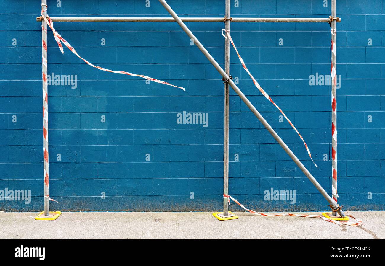 Gerüstleisten mit rot-weißem Warnband vor der blau gestrichenen Außenrandmauer Stockfoto