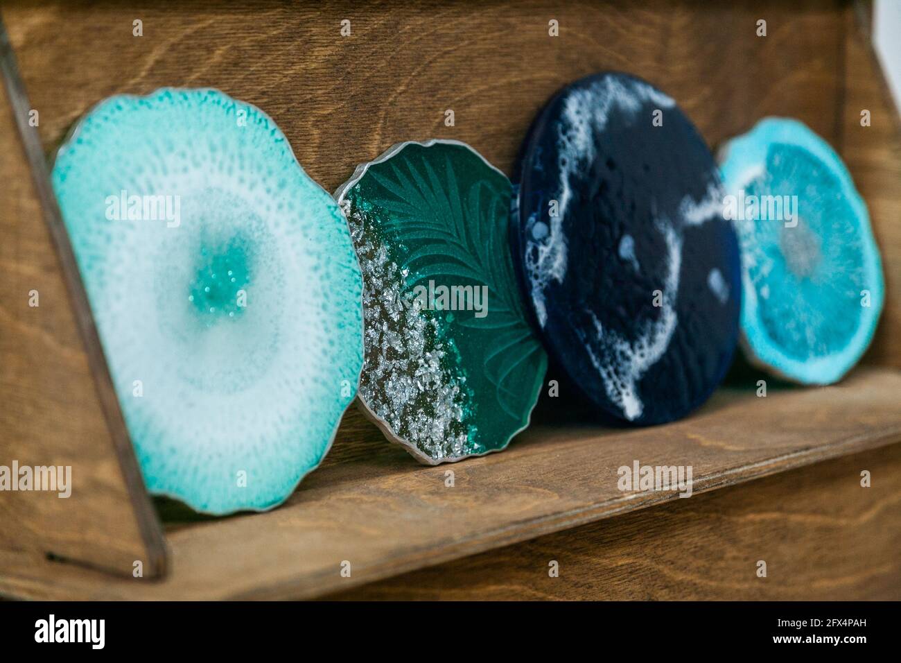 Die grünen und blauen Untersetzer sind aus Epoxidharz gefertigt. Ständer, Tablett oder dekoratives Element auf Holzregal. Stockfoto