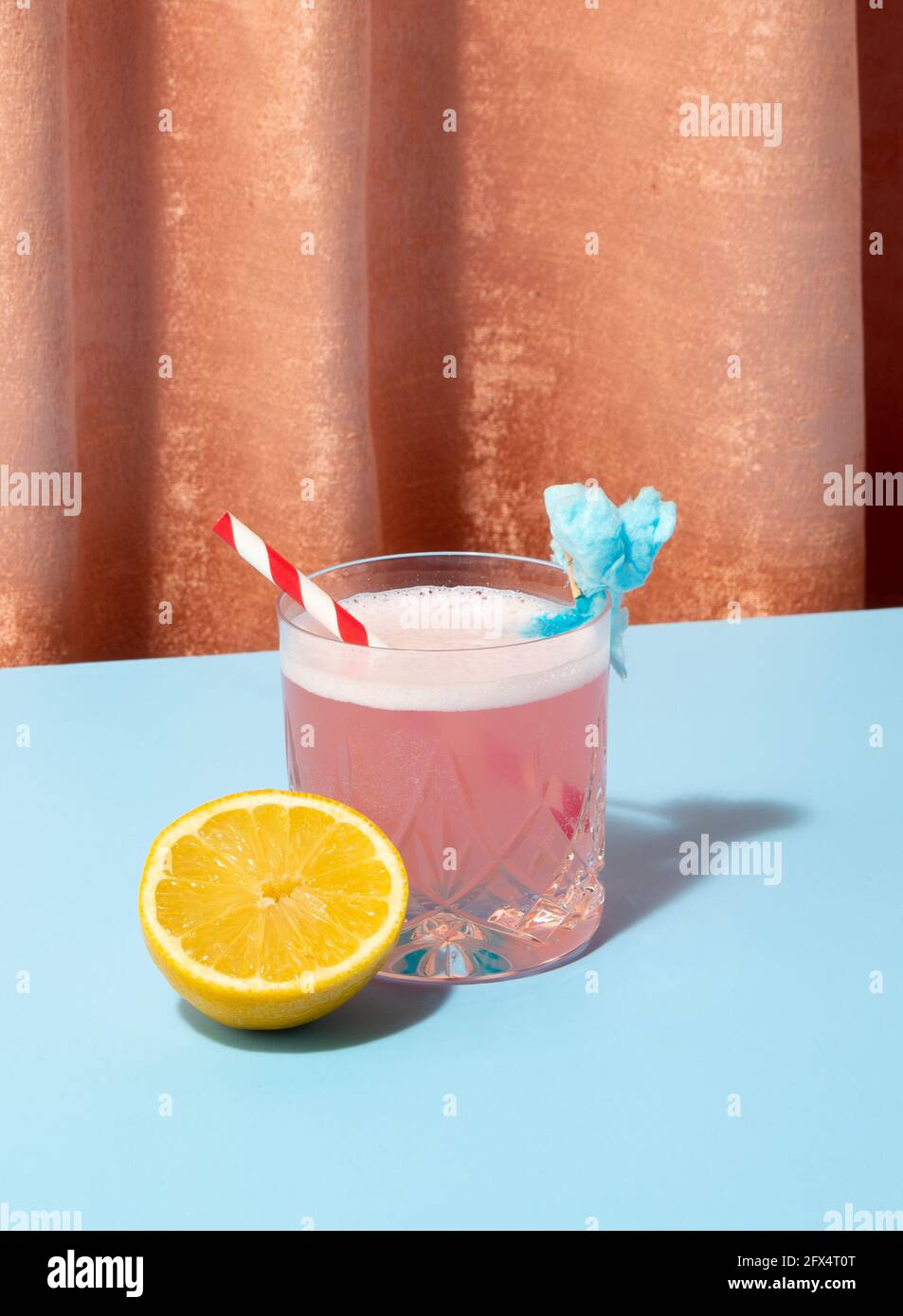 Lustiger Cocktail-Drink für eine Party auf farbigem Hintergrund. Samtig und hellblau. Zitrone und Stroh mit Lichtreflexen. Stockfoto