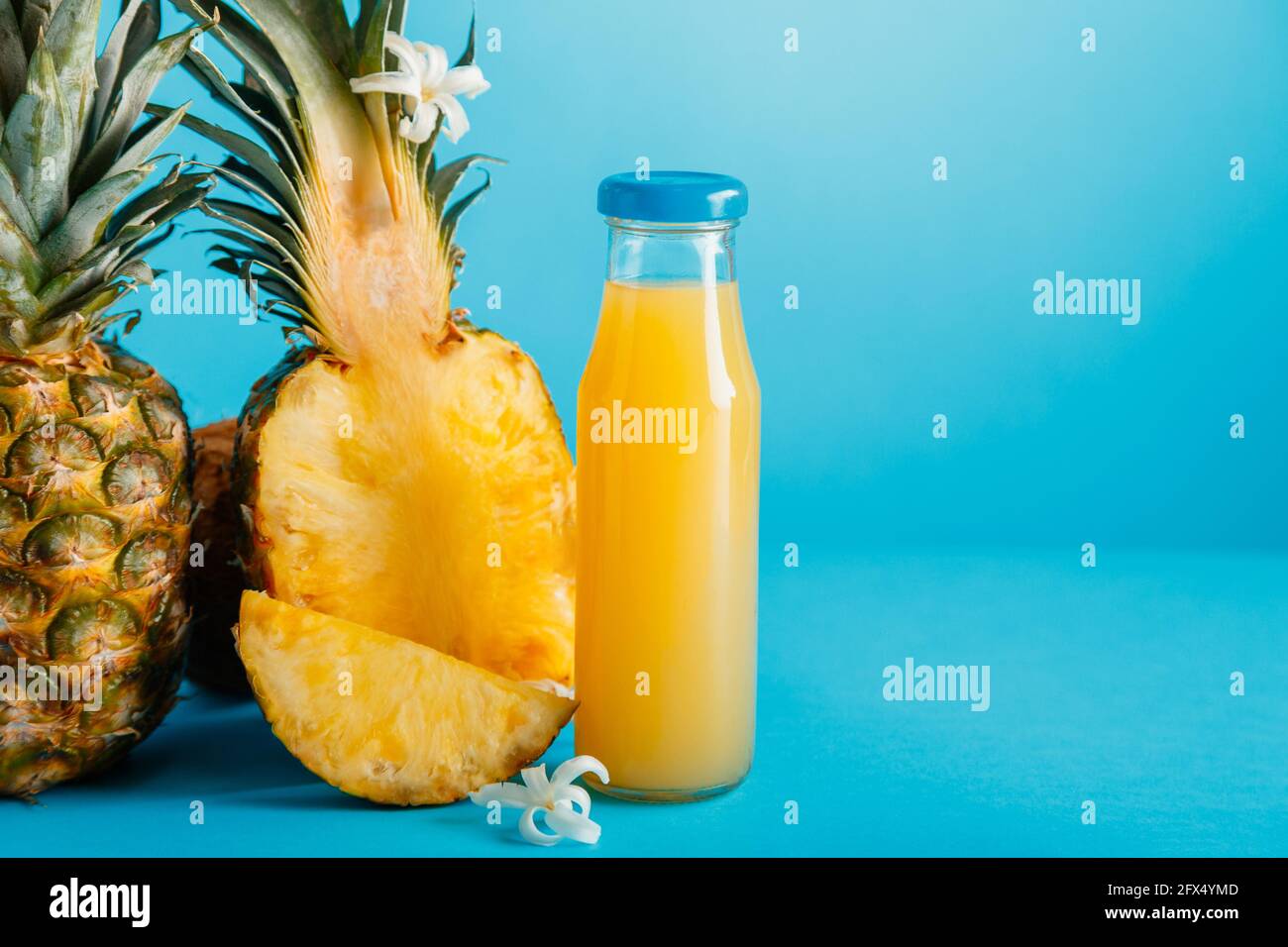 Leckere Ananassaft in Glasflasche mit Zutaten Blumen auf Blau Farbe Sommer Hintergrund Copy space. Frisches natürliches Ananasgetränk, Ananas ju Stockfoto
