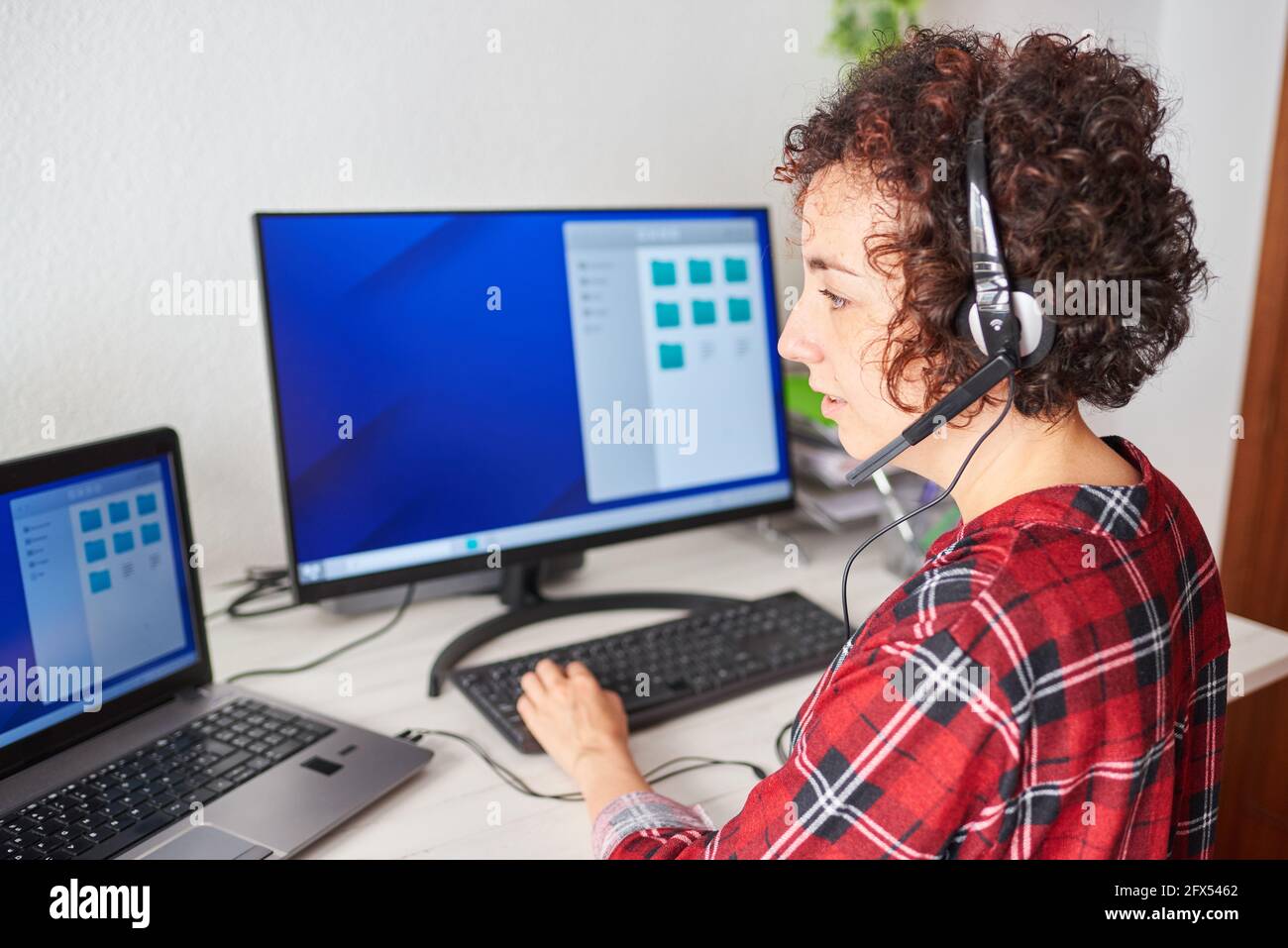 Frau, die aus der Ferne arbeitet, steht auf, trägt ein Headset und tippt auf der Tastatur Stockfoto