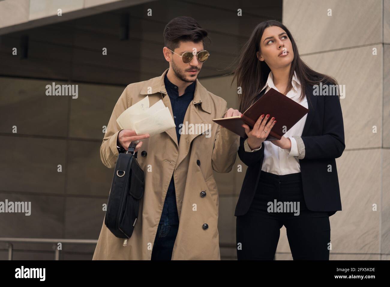 Die Chefin schaut und denkt inzwischen über die Pläne nach Ihre Assistentin prüft die Pläne in ihrem Notizbuch Stockfoto