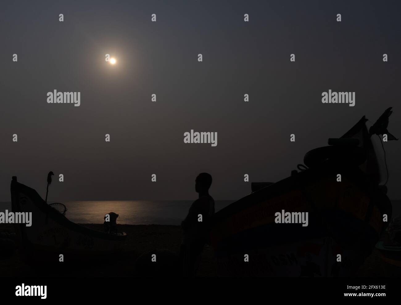 Das Bild wird am Meeresstrand aufgenommen, wenn das Mondlicht leuchtet Schatten des Fischers und seines Bootes Stockfoto